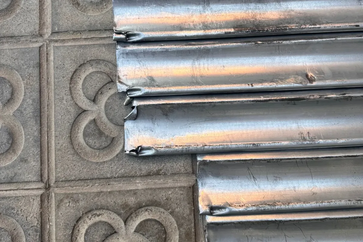 Lamas de una puerta enrollable dobladas, en el suelo sobre el panot de flor de una acera de Barcelona